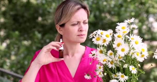 Woman with hay fever smelling chamomile flowers and dripping nose with drops in vial outside 4k movie. Seasonal allergies and bronchial asthma concept - Footage, Video
