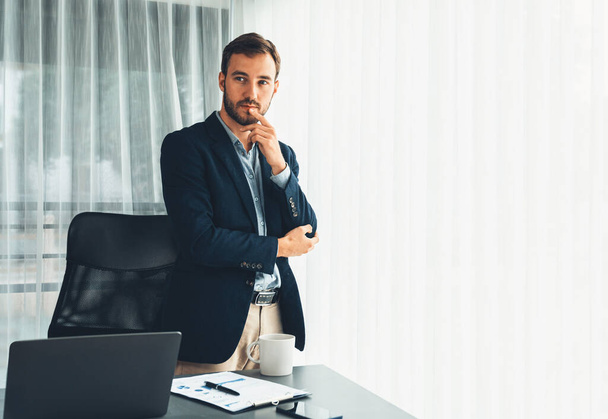 Красивый бизнесмен в черном костюме уверенно стоит на своем современном офисном портрете, глубоко задумавшись о бизнесе с задумчивым взглядом, думая стратегически о своем следующем шаге. Сущность - Фото, изображение