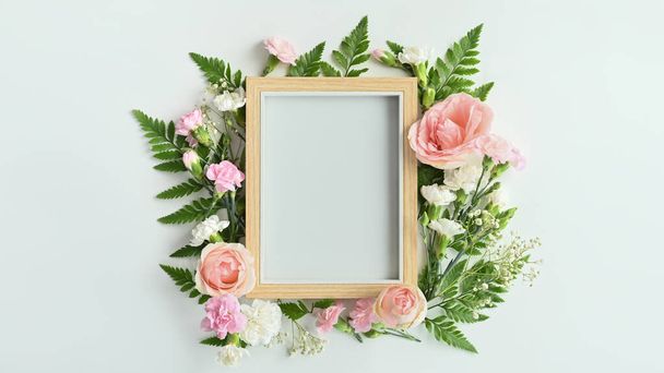 Wooden picture frame with pink rose, carnation and fern leaves on white background. Spring floral background, copy space. - Photo, image