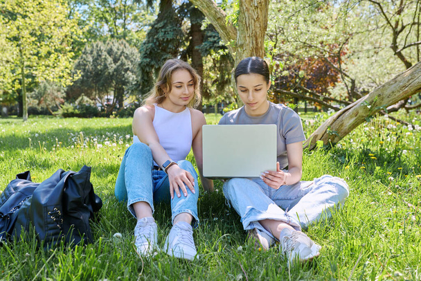 Two teen girls college high school students sitting in park on grass looking at laptop. Technologies for leisure communication, study, internet online services, e-shopping - Fotoğraf, Görsel