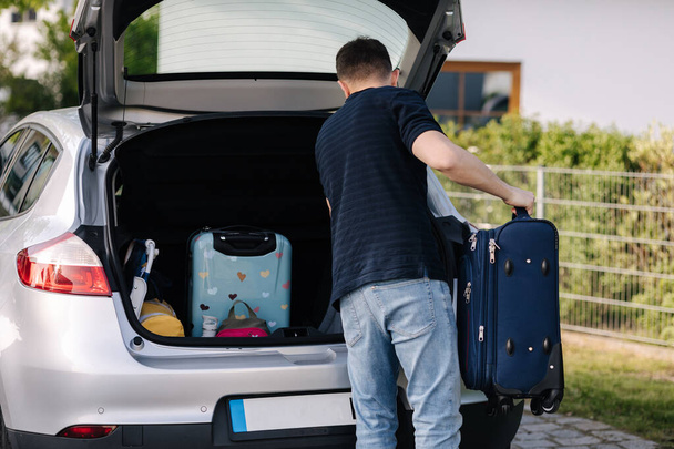 Handsome young man taking luggage baggage and other belongings from the car travel. Preparing for journey . High quality photo - Foto, imagen
