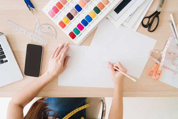 Top view egy női divattervező vagy varrónő kezét vázlatos az új design gyűjtemény papíron minták szövetek az asztalon. Divattervező egy kis üzleti koncepción dolgozik. - Fotó, kép