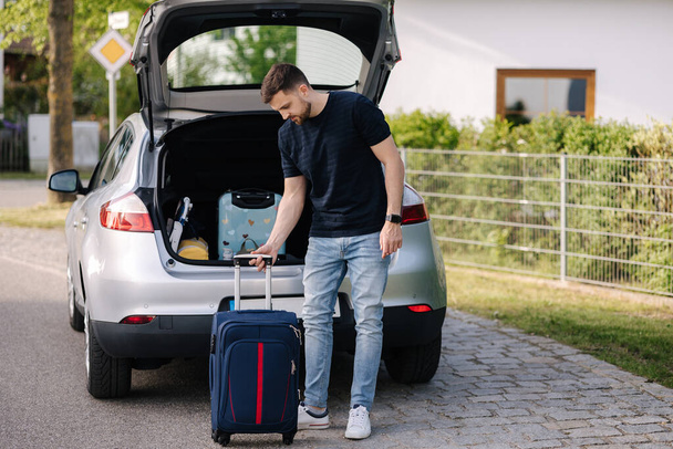 Handsome bearded man stand in front of open car trunk. Travel road trip. Holiday on summer vacation concept. High quality photo - Photo, Image