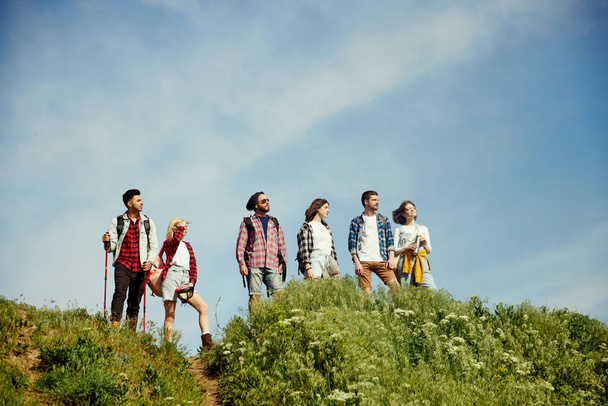Grupo de amigos caminando en el prado en un día cálido, soleado y de verano. Jóvenes de pie en la colina y disfrutando de la naturaleza, el paisaje. Concepto de estilo de vida activo, naturaleza, deporte y hobby, amistad - Foto, imagen