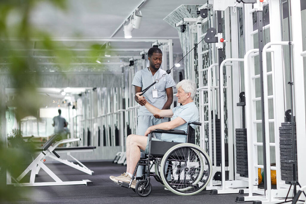 Retrato de vista lateral del hombre mayor en silla de ruedas haciendo ejercicios en el gimnasio en la clínica de rehabilitación, espacio para copiar - Foto, Imagen