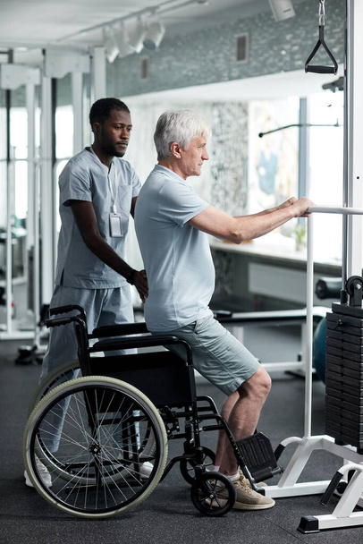 Retrato completo del hombre mayor haciendo ejercicios de rehabilitación en el gimnasio de la clínica médica con la asistencia de terapeuta - Foto, Imagen