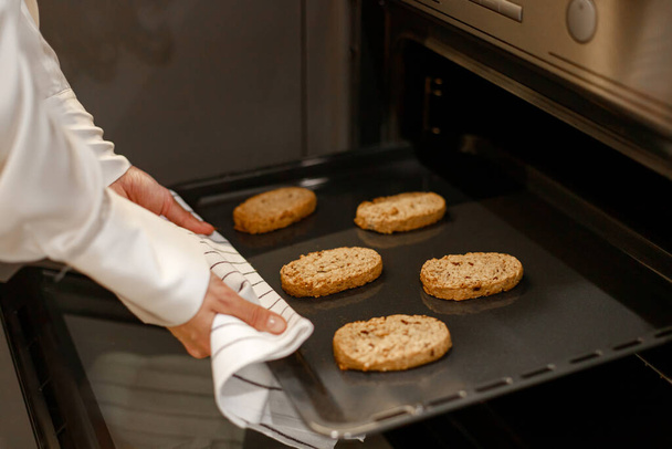 Foto ritagliata di mani casalinghe che prendono la teglia con i biscotti di farina d'avena fuori dal forno. Concetto di cibo e cucina - Foto, immagini