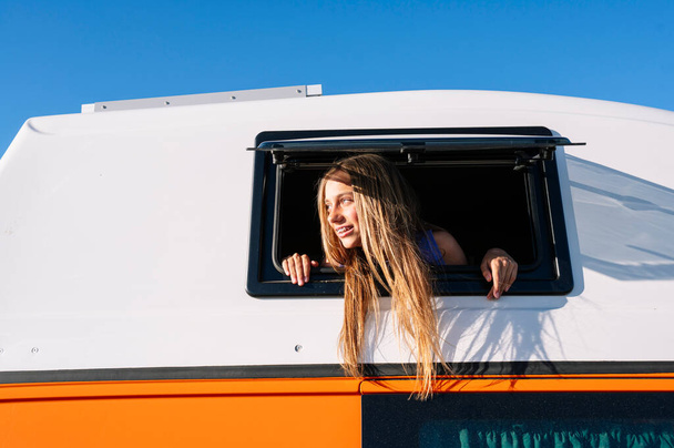 Το χαρούμενο κορίτσι βγάζει το κεφάλι της από το παράθυρο του φορτηγού μια υπέροχη μέρα στην κατασκήνωση. Έννοια ζωής Van. - Φωτογραφία, εικόνα