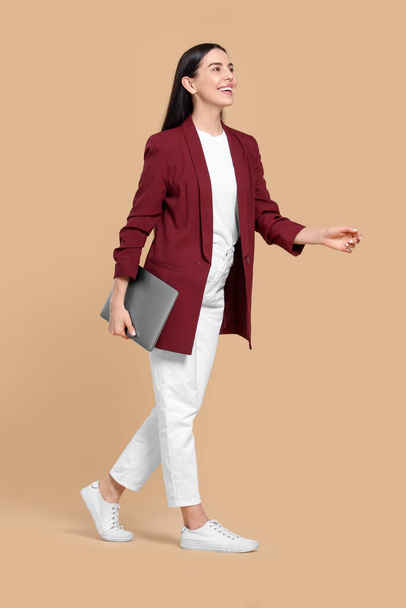 Happy woman with laptop walking on beige background - Foto, Bild
