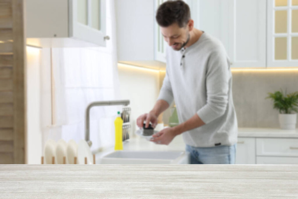 Man doing washing up in kitchen, focus on empty wooden table - Φωτογραφία, εικόνα