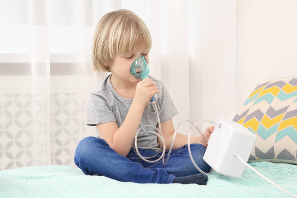 Sick little boy using nebulizer for inhalation on bed at home - Foto, imagen