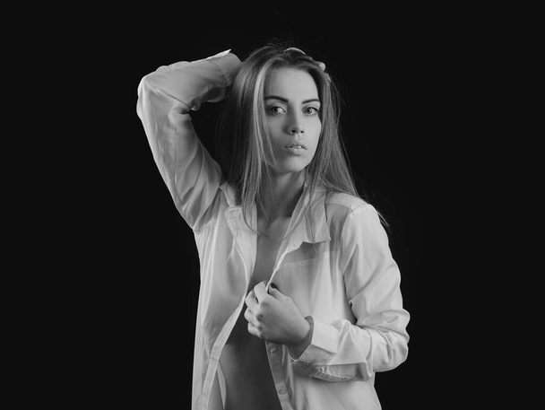 Portrait of young attractive woman in shirt. Dramatic and sensual portrait of a beautiful girl isolated on a dark background in studio - Foto, afbeelding