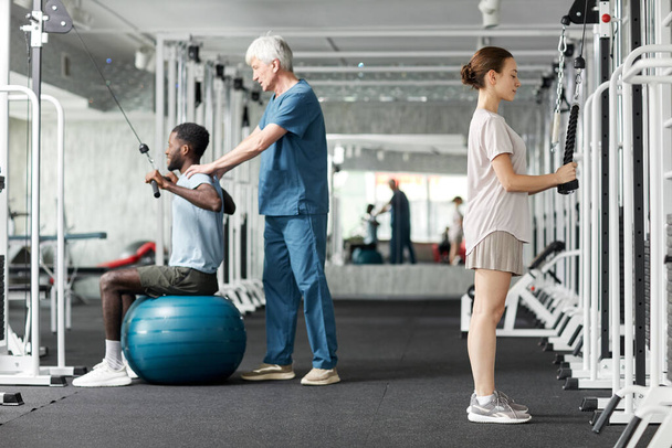 Retrato completo de personas que utilizan máquinas de fisioterapia en el gimnasio en la clínica de rehabilitación - Foto, imagen
