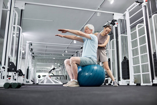 Ritratto di giovane terapista donna che assiste l'uomo anziano a fare esercizi fisici in clinica di riabilitazione, copiare lo spazio - Foto, immagini