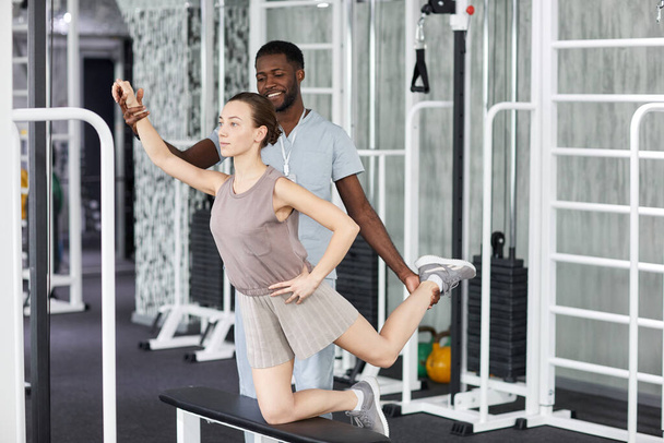 Retrato de larga duración de una mujer joven haciendo ejercicios de fisioterapia en el gimnasio en la clínica de rehabilitación con el médico masculino asistiendo - Foto, Imagen