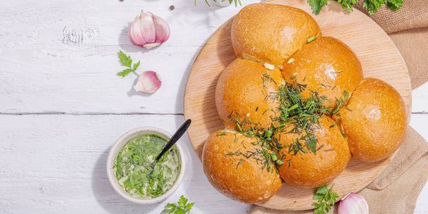 Aromatic garlic buns. Fresh baked goods, a traditional gluten-free soup snack. Parsley, spices, olive oil. Hard light, dark shadow, white wooden background, banner format - Foto, imagen