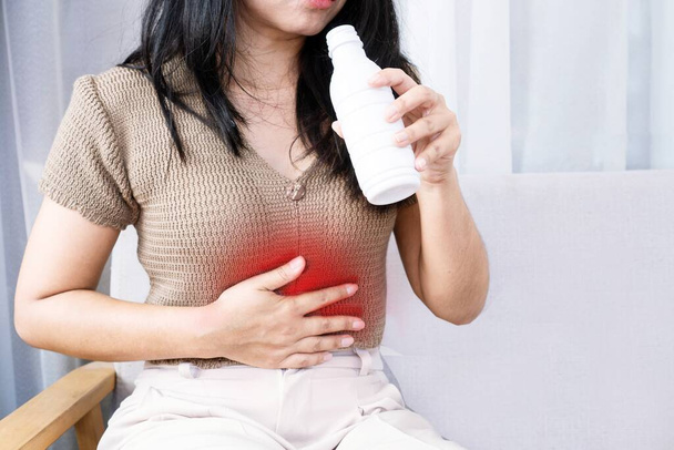Azjatka przyjmująca lek zobojętniający sok żołądkowy w leczeniu zgagi wywołanej niestrawnością i bólem brzucha - Zdjęcie, obraz