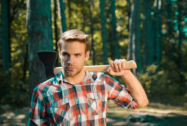 Lumberjack on serious face carries axe on shoulder. Bearded man with axe concept. Lumberjack with axe on forest background. Man doing mans job. Harvest of timber - Fotoğraf, Görsel