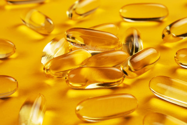 Fish oil capsules with omega 3 and vitamin D on yellow background. - Foto, imagen