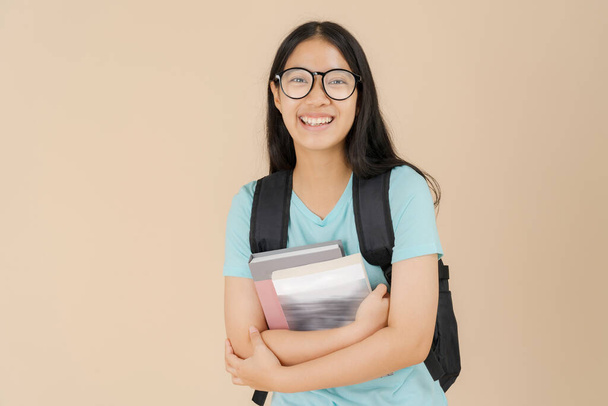 Een gelukkige Aziatische studente draagt een bril en draagt een boek - Foto, afbeelding