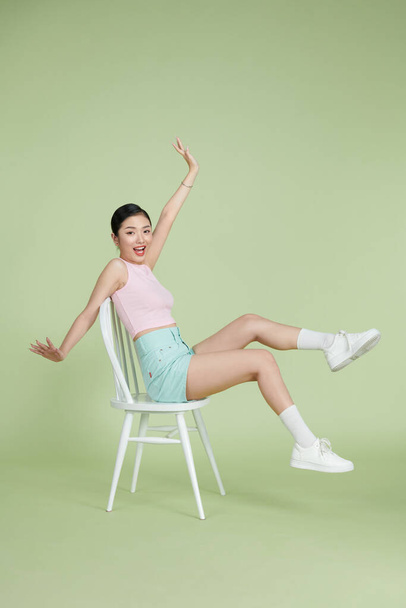 Photo of sweet excited woman smiling rising arms sitting chair isolated on green background - Foto, Imagem