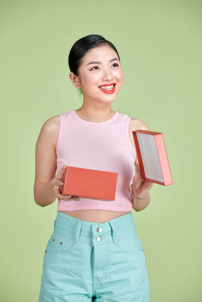 Happy young woman opening present for Valentine's Day on green studio background,  - 写真・画像