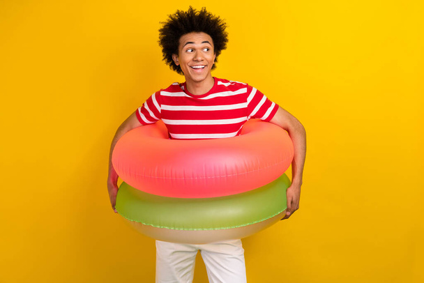 Photo of excited dreamy guy wear striped t-shirt two floating rings looking empty space isolated yellow color background. - Foto, Imagem