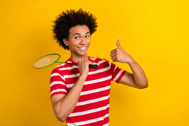 Photo of funny confident guy dressed red t-shirt playing badminton showing thumb up isolated yellow color background. - Photo, Image