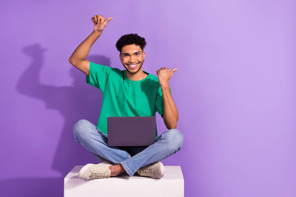 Full body photo of young man wear green t-shirt direct fingers empty space with laptop sit box netbook apps isolated on purple background. - Foto, imagen