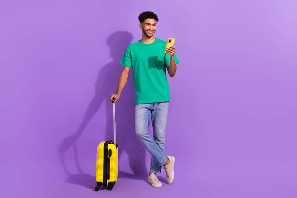 Full body photo of young man browsing phone wear stylish clothes booking hotel reservation with luggage isolated on violet color background. - Foto, Imagem