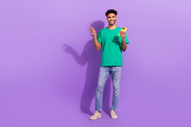 Full body photo of young man blog wear trendy clothes pointing finger empty space phone website promo isolated on purple color background. - Valokuva, kuva