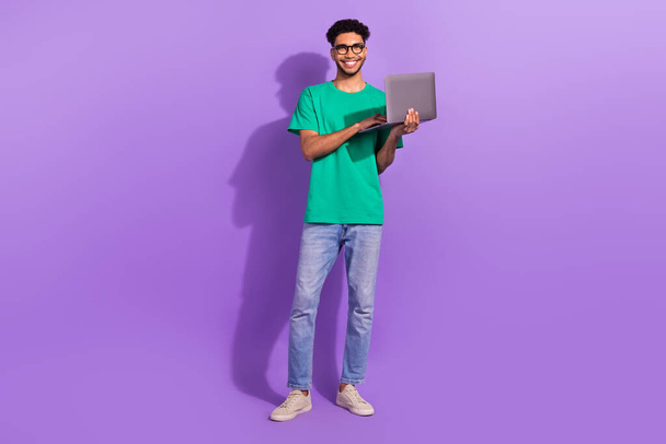 pleine longueur photo de jeune étudiant gars porter des lunettes tenir ordinateur portable étudier le codage futur programmeur réussi isolé sur fond violet. - Photo, image