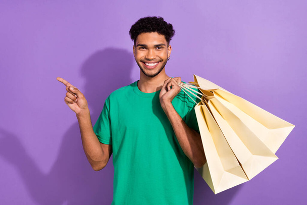 Photo of funny handsome man hold boutique bags indicate finger empty space isolated on violet color background. - Fotó, kép
