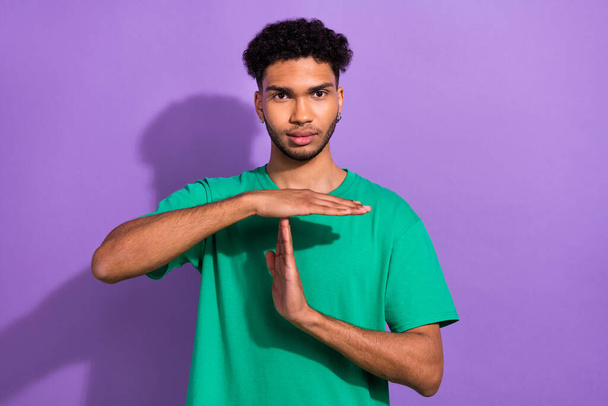 Photo of serious confident guy dressed green t-shirt showing time out gesture isolated violet color background. - Foto, afbeelding