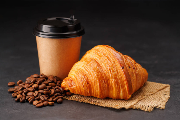 Aromatic coffee in a paper cup paired with a flaky croissant. With copy space - Photo, Image