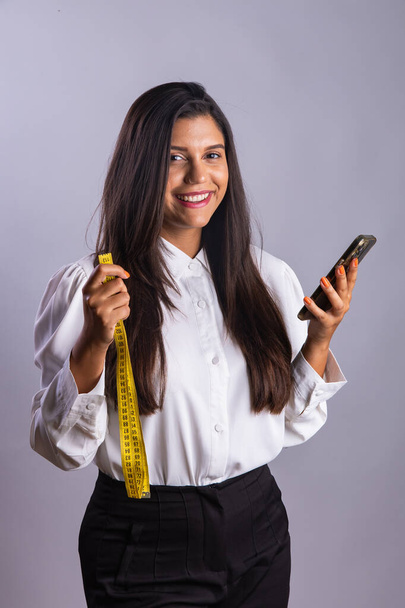 Brazilian woman, nutritionist, holding measuring tape and smartphone. - Фото, изображение