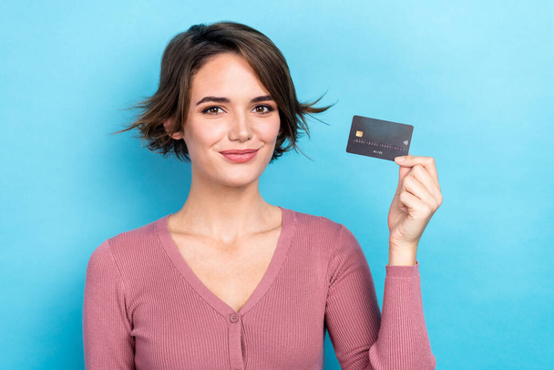 Photo of cheerful positive lady wear pink cardigan smiling rising bank card isolated blue color background. - Фото, зображення
