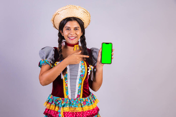 Brazilian woman, clothes from Festa Junina, Arraial, Festa de Sao Joao. with smartphone, green screen. - Fotografie, Obrázek