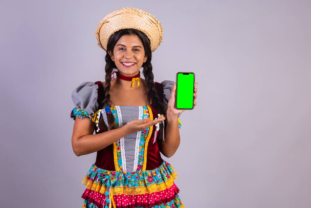 Brazilian woman, clothes from Festa Junina, Arraial, Festa de Sao Joao. with smartphone, green screen. - Photo, image