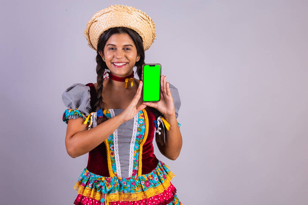Brazilian woman, clothes from Festa Junina, Arraial, Festa de Sao Joao. with smartphone, green screen. - Foto, Imagem