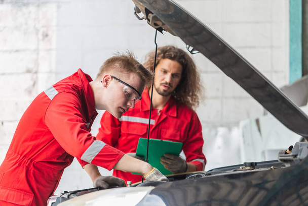 Technician team checking modern car at garage, Young Caucasian car mechanic with a checklist, Mechanics in uniform are working in auto service, Car repair and maintenance - Foto, immagini