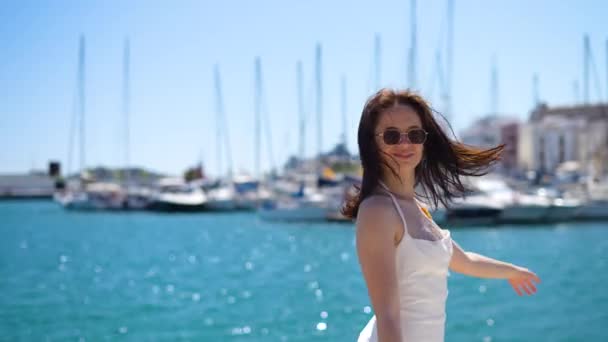 Chica en vestido blanco permanecer embarcaciones costa fondo mirando a la cámara y disfrutar. Imágenes de alta calidad 4k - Metraje, vídeo