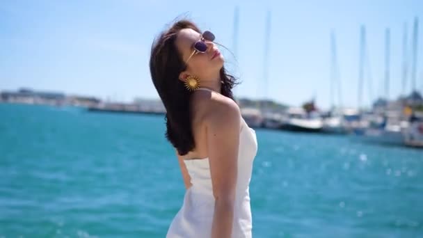 Lány fehér ruha és napszemüveg a kikötőben, nézi a kamerát, és élvezze. Kiváló minőségű 4k felvételek - Felvétel, videó