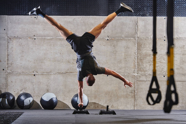 A muscular man in a handstand position, showcasing his exceptional balance and body control while performing a variety of exercises to enhance his overall body stability and strength in a modern gym. - Foto, immagini
