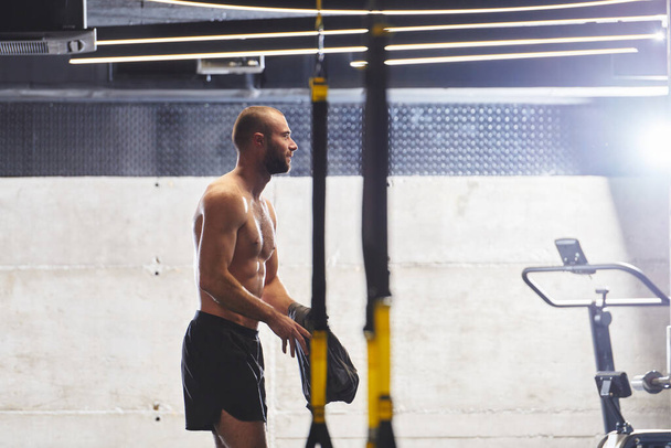 Svalnatý muž v tělocvičně, připravuje se na cvičení, vyzařuje odhodlání a soustředění, jak se připravuje posunout své limity a dosáhnout svých fitness cílů - Fotografie, Obrázek