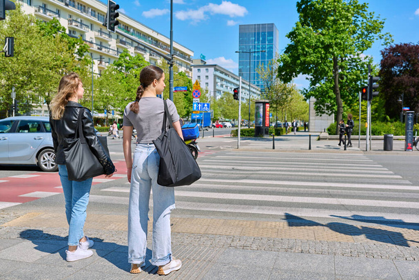 Young women cross the road at a pedestrian crossing, in a modern European city. Urban style, lifestyle, people concept - 写真・画像