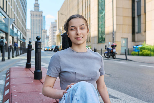 Young smiling teenage girl looking at camera on street of modern European city. High school age, adolescence, fashion style youth lifestyle concept - Photo, Image