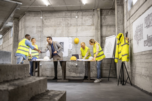 Team of structural engineers and architects analyzing plans and blueprints at construction site. - Photo, image