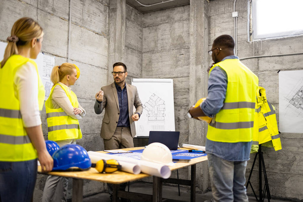 Team of structural engineers and architects having a meeting at construction site analyzing structure plant or blueprint. - Φωτογραφία, εικόνα