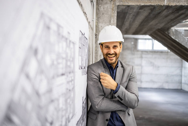 Engenheiro de construção caucasiano alegre em pé no local de construção e sorrindo para a câmera. - Foto, Imagem